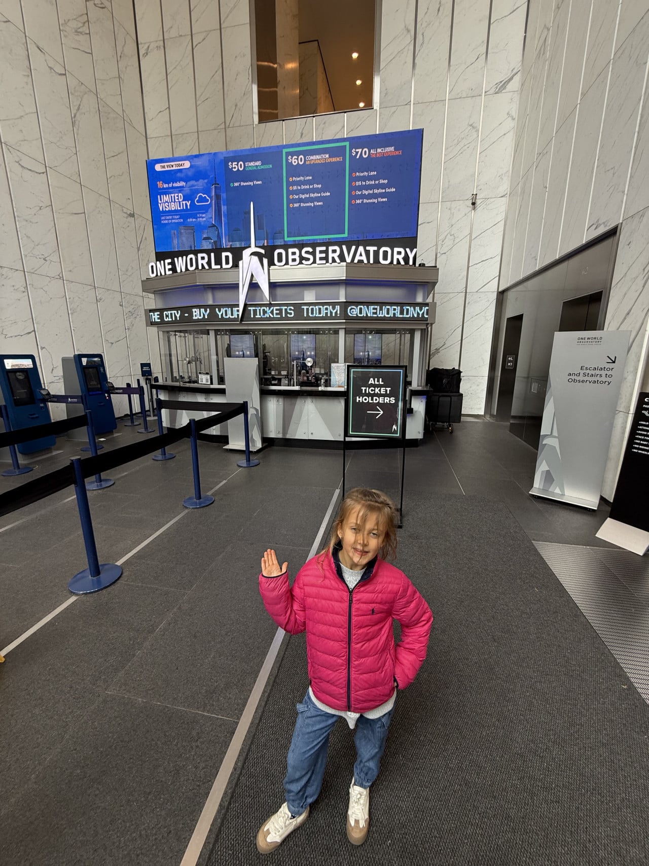 Dívka v růžové bundě stojí u pokladen One World Observatory v New Yorku.
