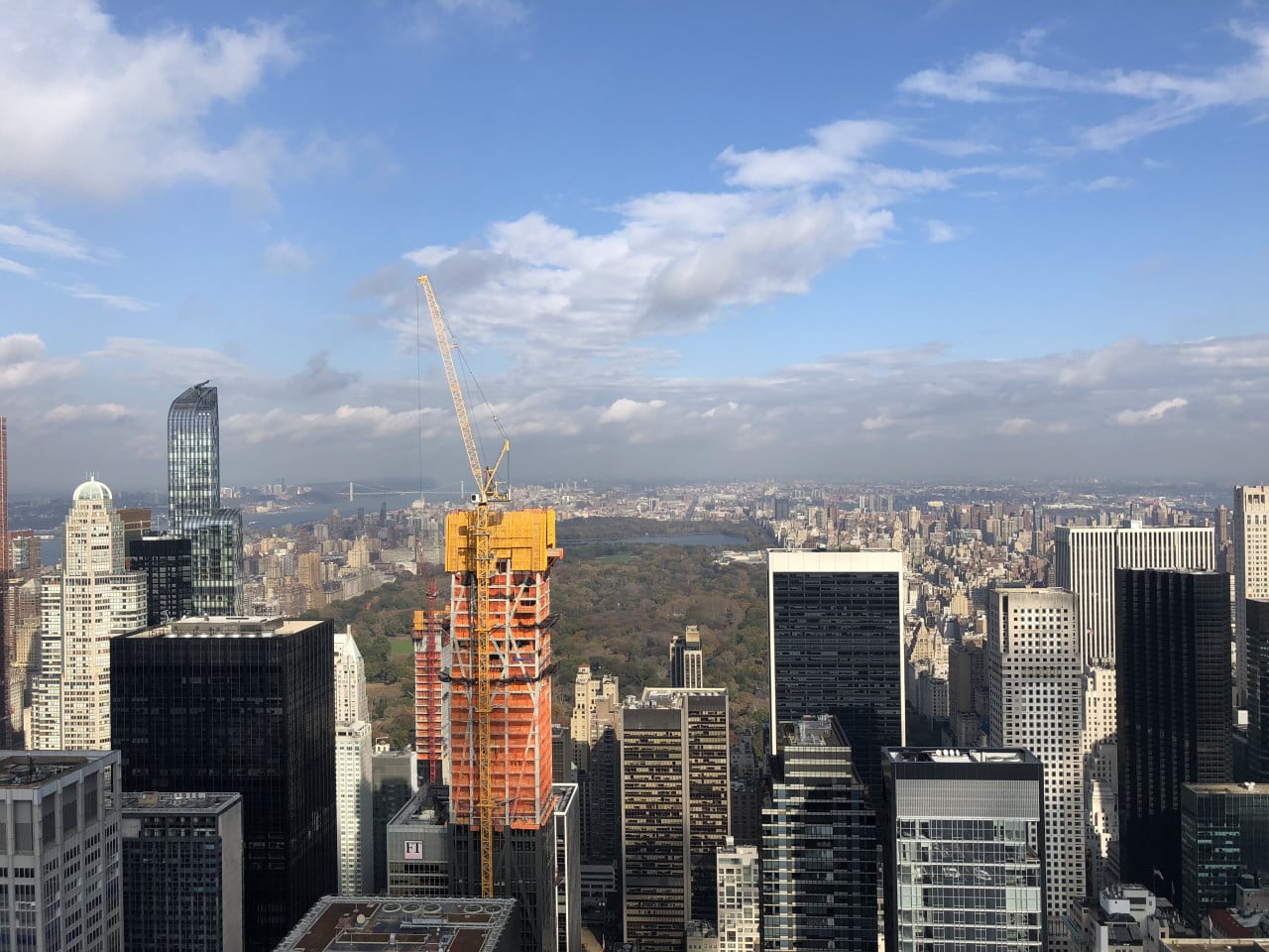 Pohled na Manhattan, Central Park a rozestavěnou věž s jeřábem pod modrou oblohou.