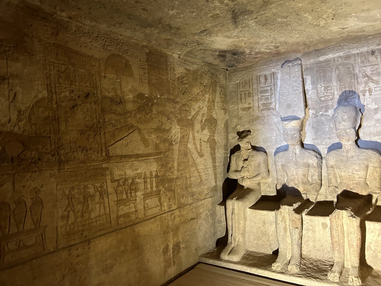Reliéf se třemi egyptskými sochami a hieroglyfy na stěně chrámu.