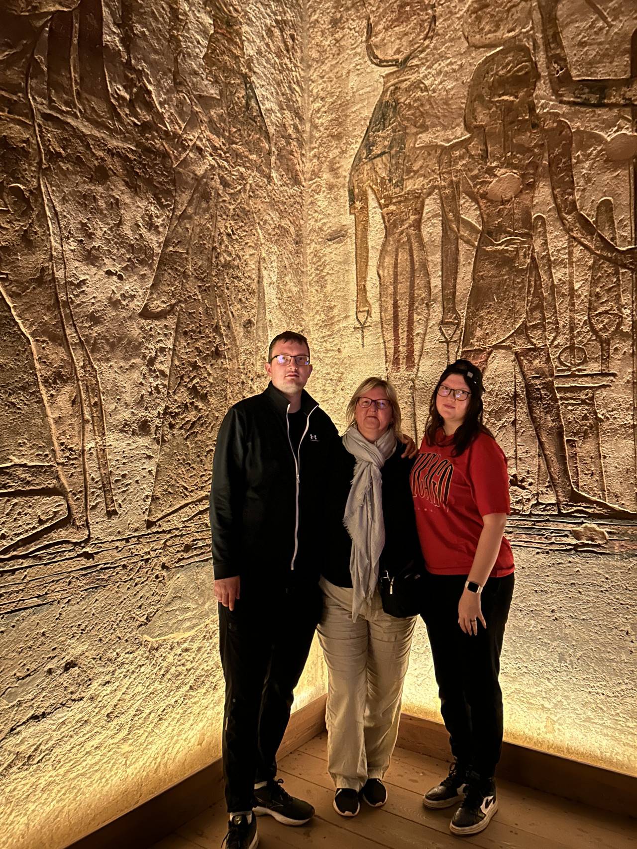 Tři lidé před reliéfní stěnou v chrámu Abu Simbel, Egypt.