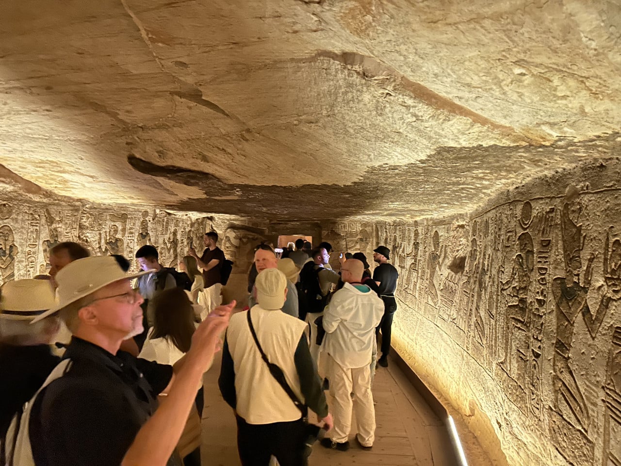 Turisté v osvětlené egyptské chodbě s reliéfy v Abu Simbelu