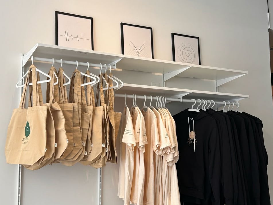 Položené tašky, trička a mikiny na bílých regálech v kamenném obchodě