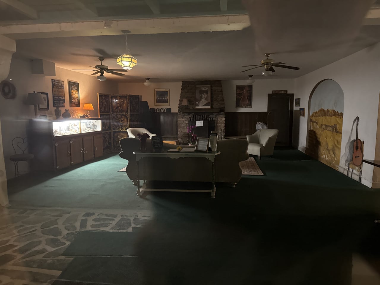 Tmavý hotelový lobby s gauči, krbem, obrazy a nápisem TODAY.