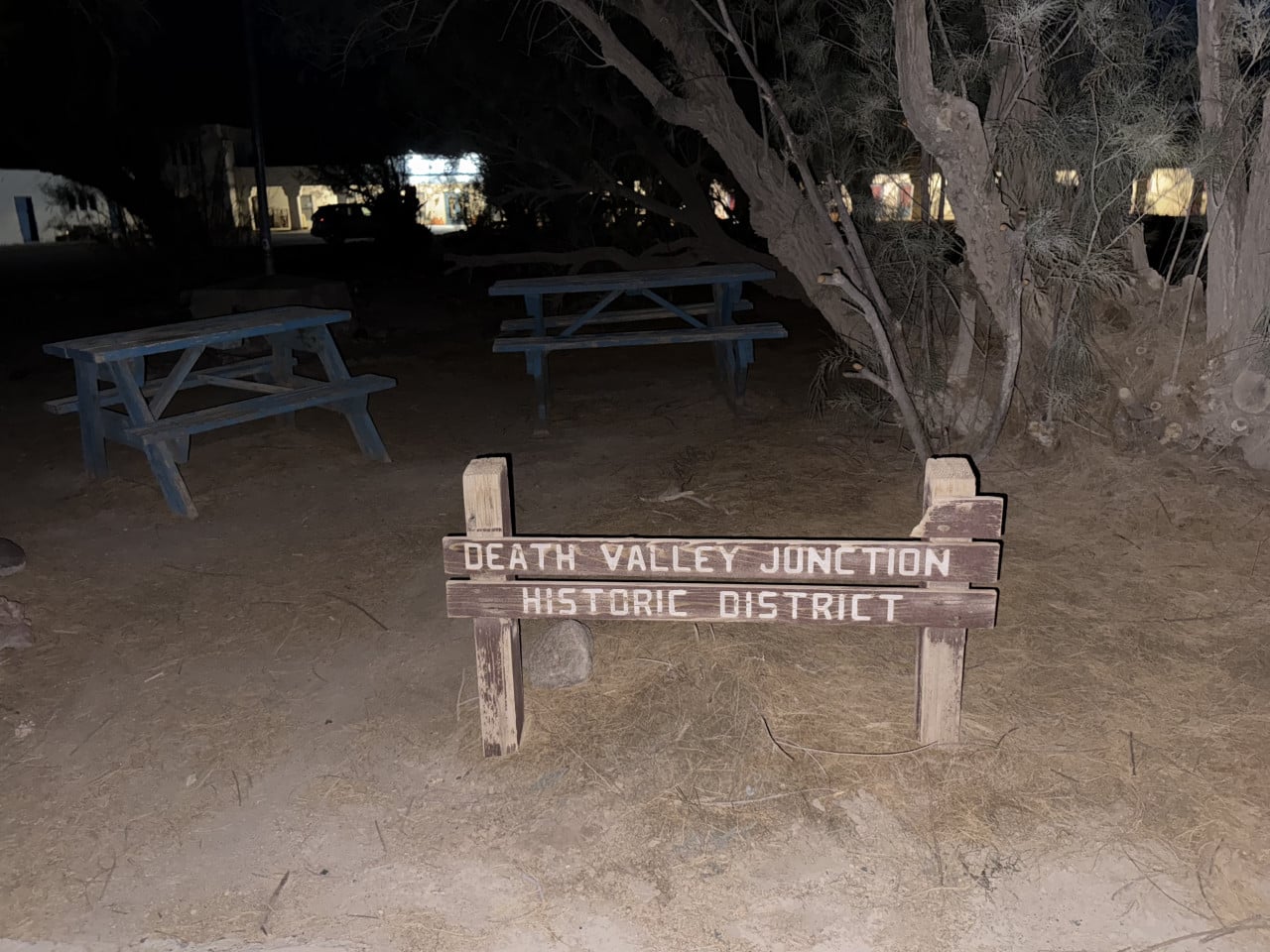Dřevěná cedule Death Valley Junction Historic District u tmavého parku s piknikovými stoly a stromy
