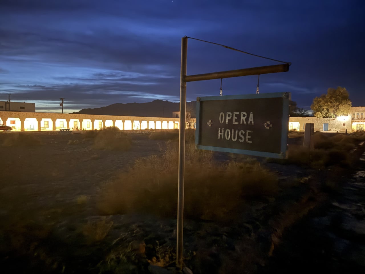 Noční exteriér Amargosa Opera House s osvětleným nápisem OPERA HOUSE v poušti