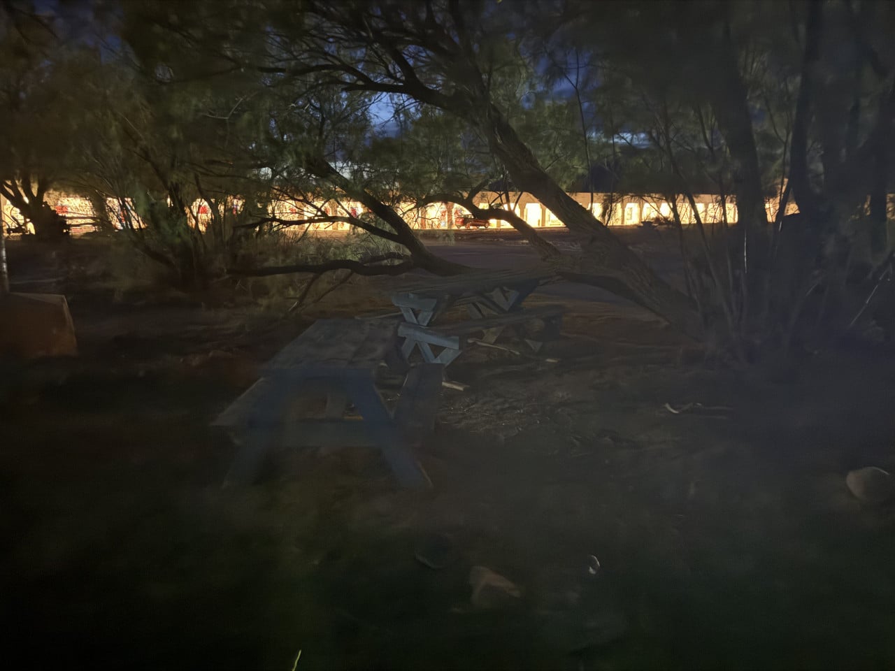 Osvětlená budova hotelu za stromy v noci, prázdná lavička v popředí