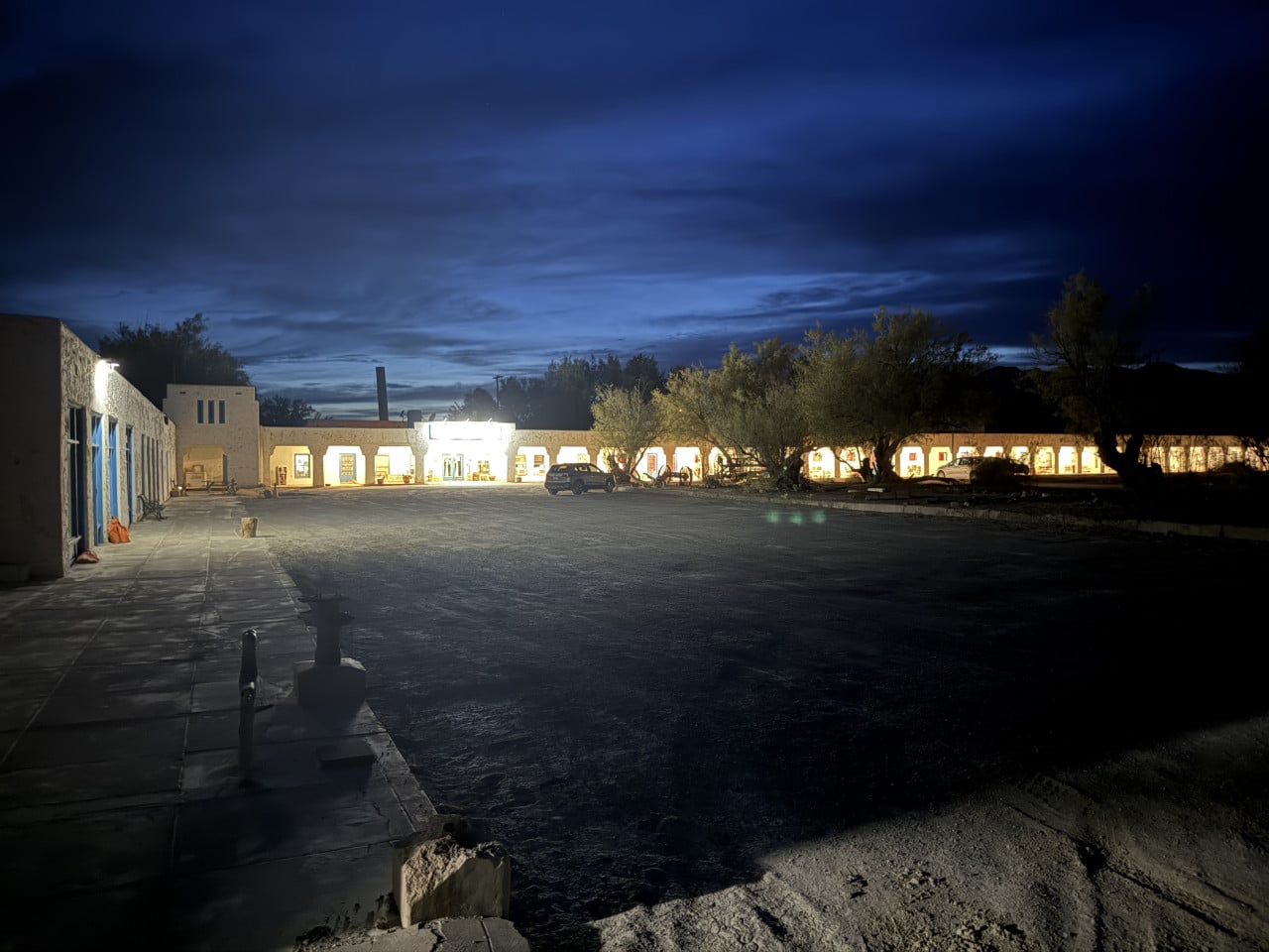 Noční osvětlené nádvoří Amargosa Opera House v poušti, obklopené budovami a stromy.