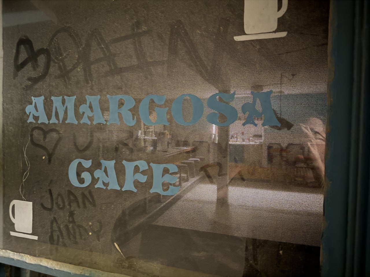 Okno Amargosa Cafe s modrým nápisem a zamlženým interiérem za sklem