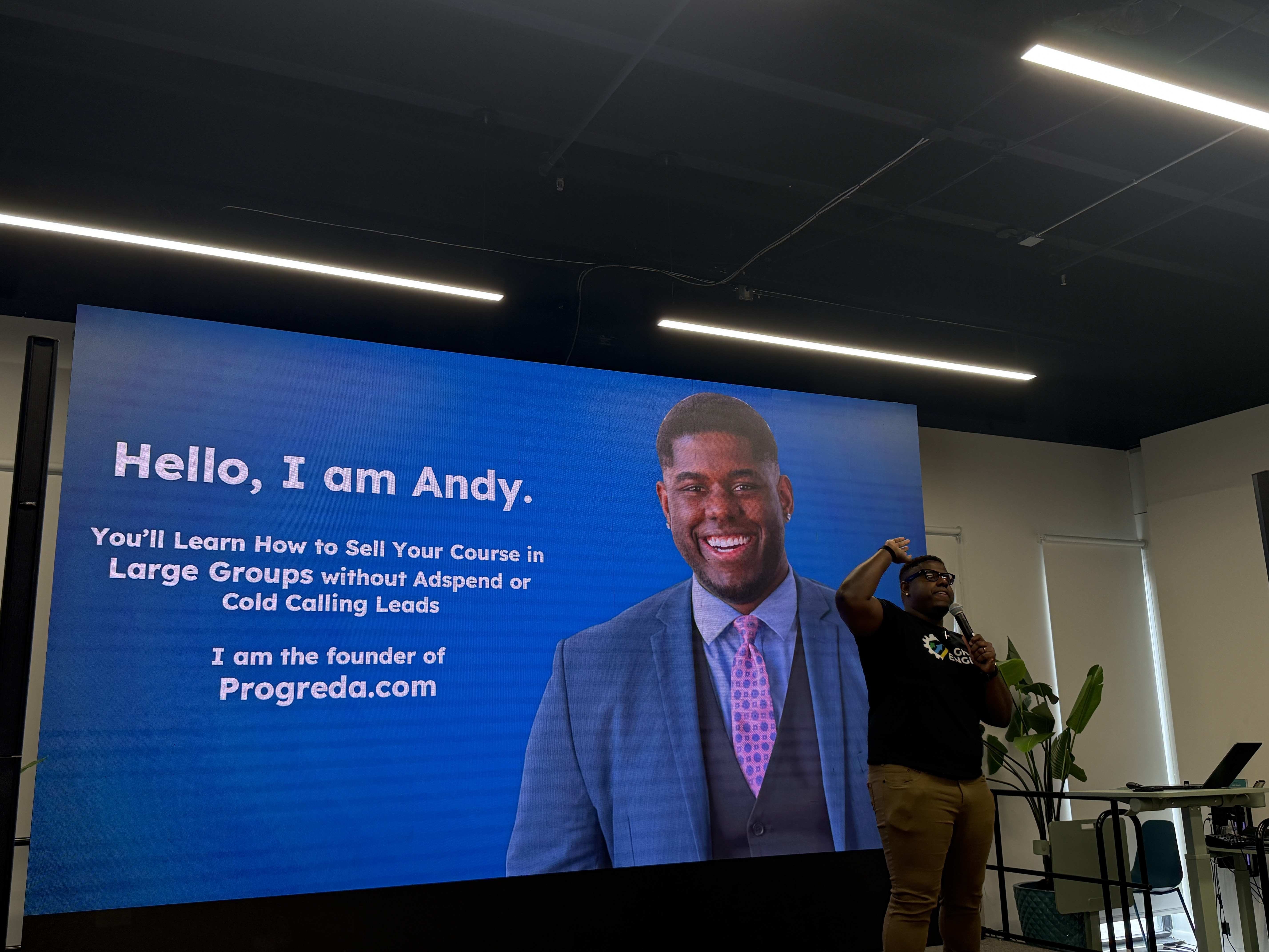 Přednášející s mikrofonem na pódiu před obrazovkou Hello, I am Andy. Progreda.com