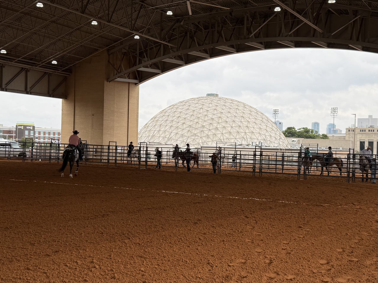 Krytá jezdecká aréna s jezdci na koních a kopulí Will Rogers Memorial Center v pozadí