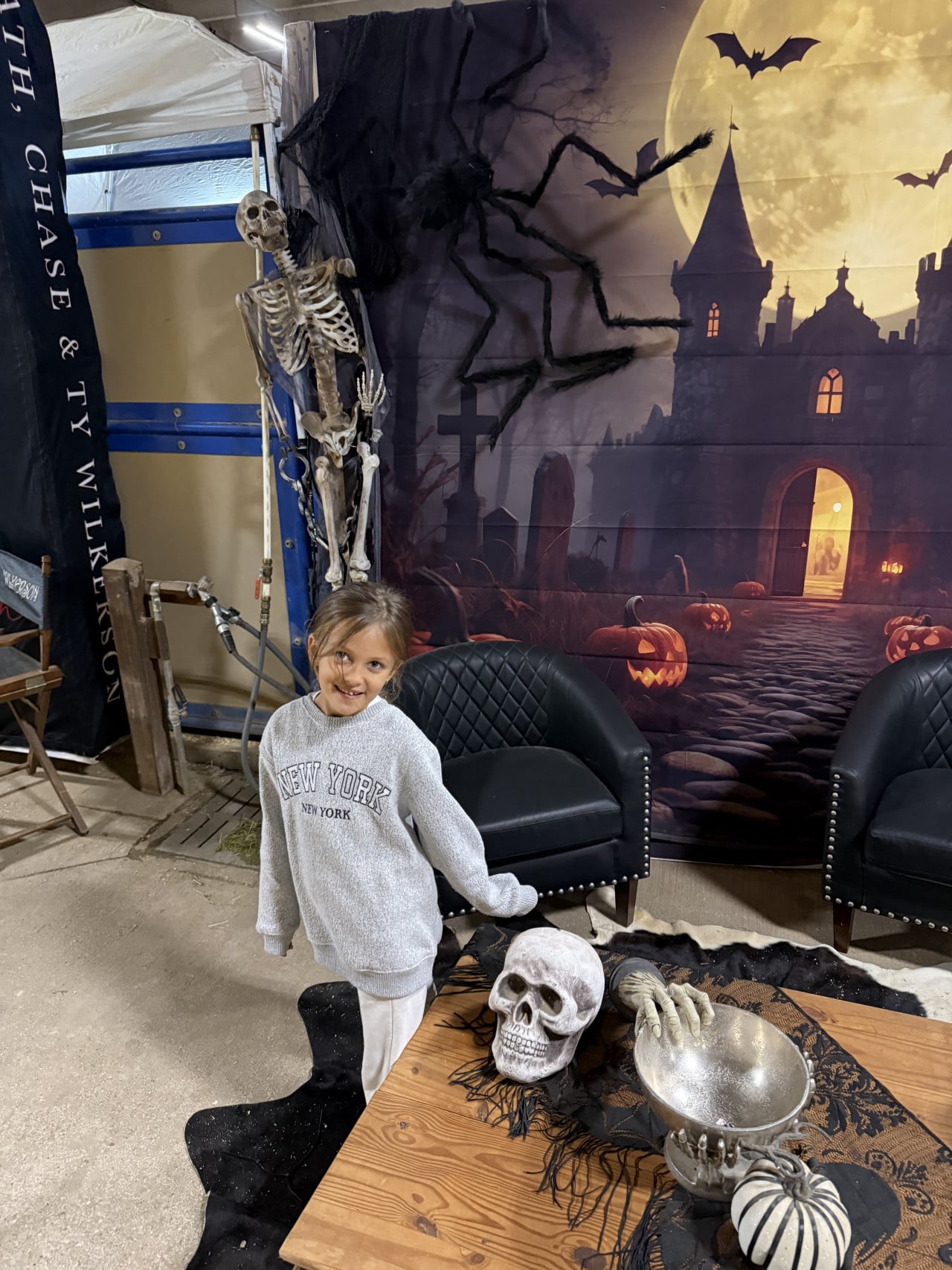 Dítě v kostýmu na halloweenské dekoraci se skeletonem, lebkami a dýněmi.