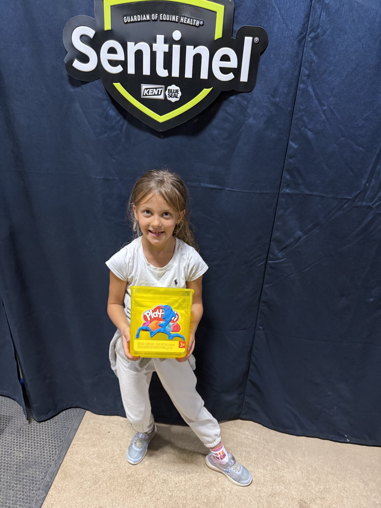 Dívka stojí před logem Sentinel a drží žlutou krabičku Play-Doh.