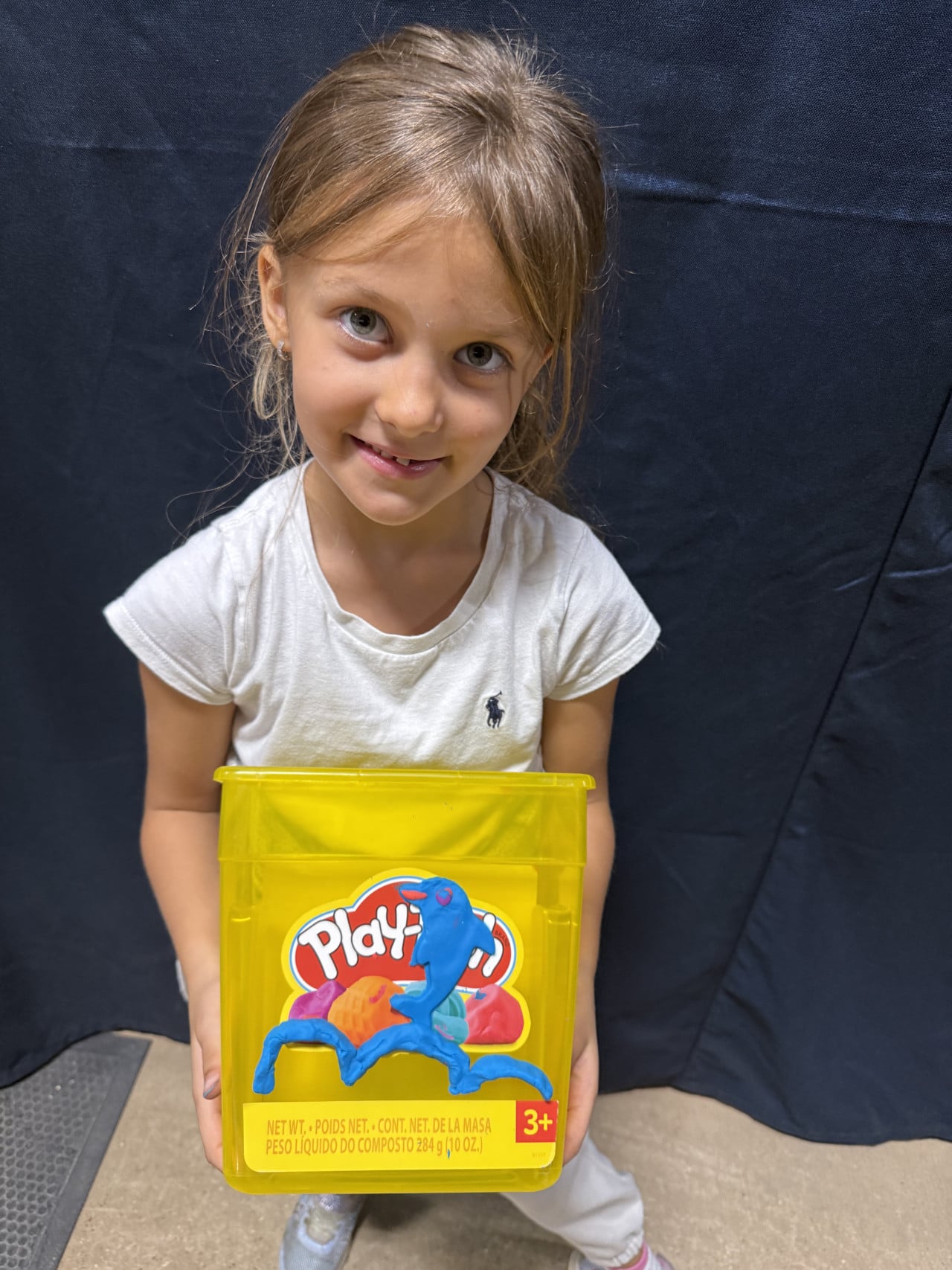Malá dívka drží žlutou krabičku Play-Doh s modrou plastelínou.