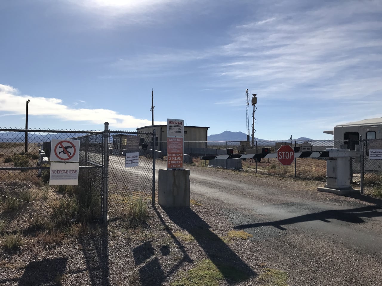Brána Area 51 s výstražnými cedulemi, stop značkou a pouštní krajinou.