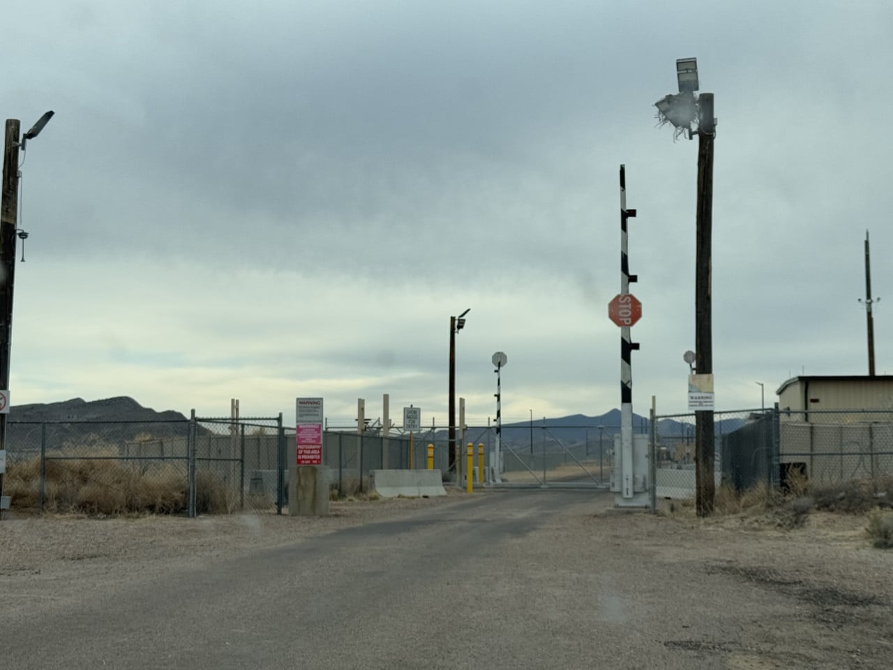 Brána a oplocený vstup do Area 51 v nevadské poušti, s varovnými cedulemi a stopkou