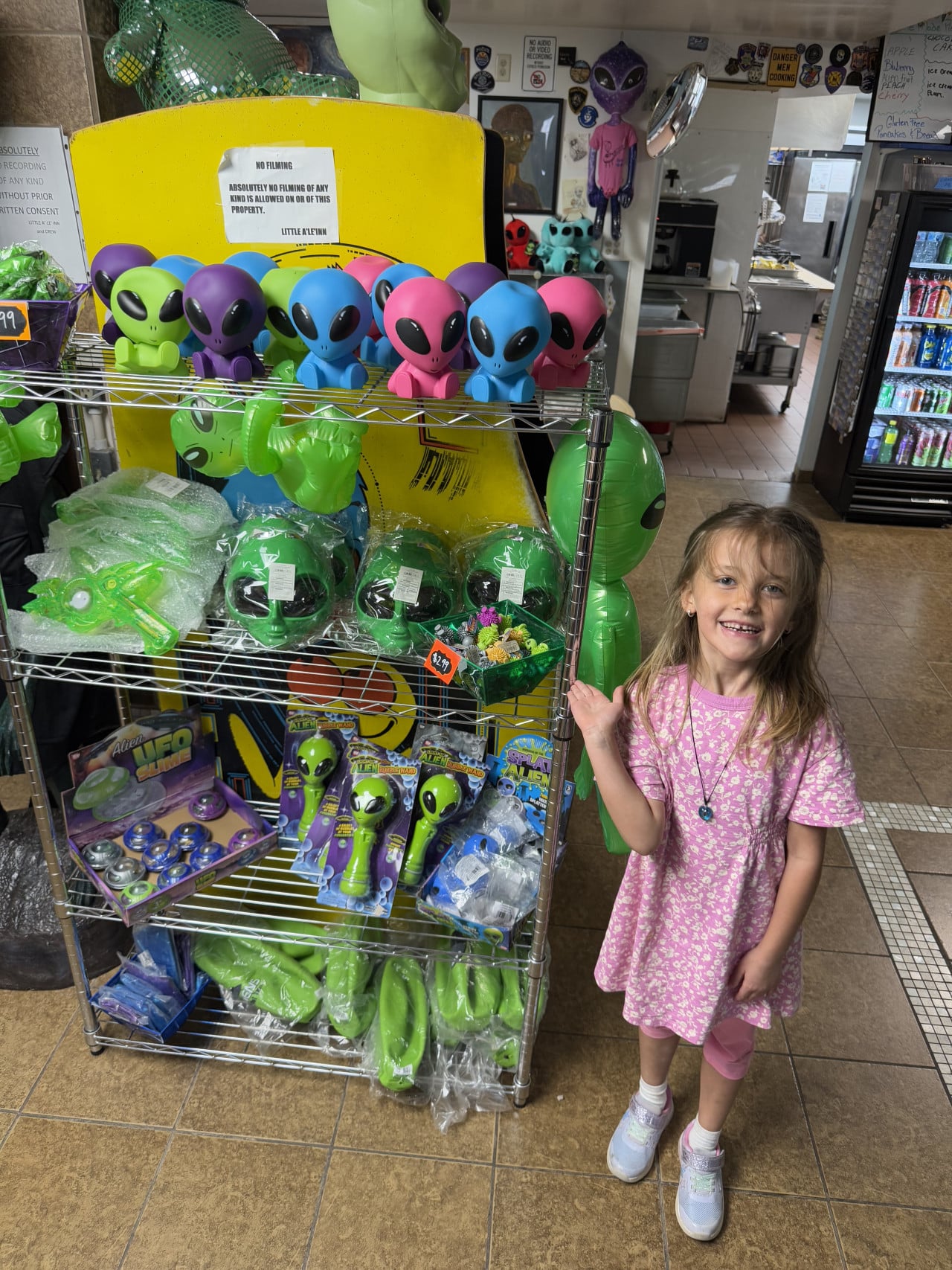 Dívka stojí u regálu s barevnými figurkami a suvenýry s motivem mimozemšťanů.