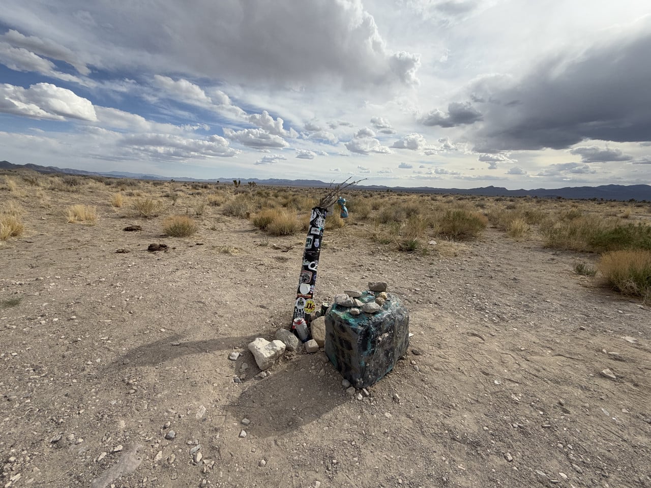 Pustá nevadská poušť s improvizovaným sloupkem oblepeným samolepkami a kamennou mohylou.