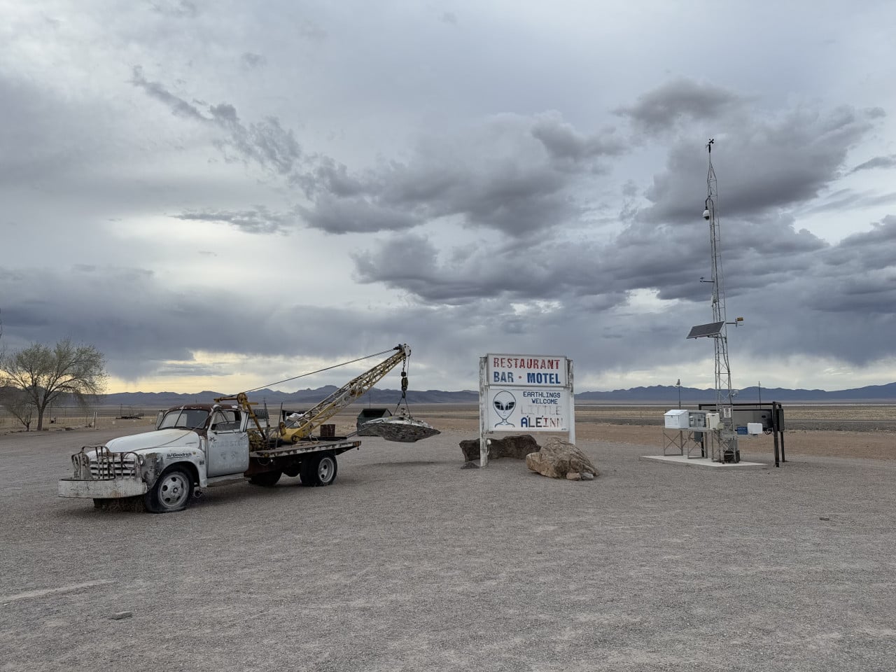 Prašná nevadská planina s odtahovým autem, nápisem Little A’Le’Inn a vysokou meteorologickou věží.