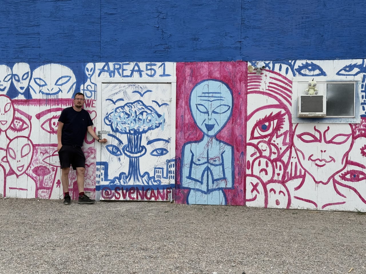 Muž stojí před barevnou stěnou s graffiti mimozemšťanů a nápisem AREA 51.