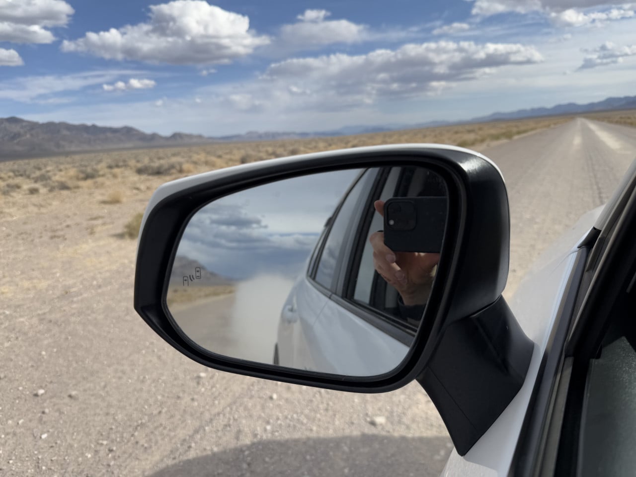 Pohled z auta na prázdnou pouštní silnici, boční zrcátko a nevadskou krajinu.