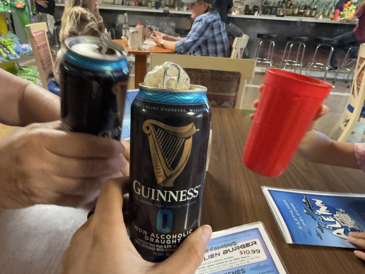 Lidé si připíjejí plechovkami Guinness a červeným kelímkem v restauraci.