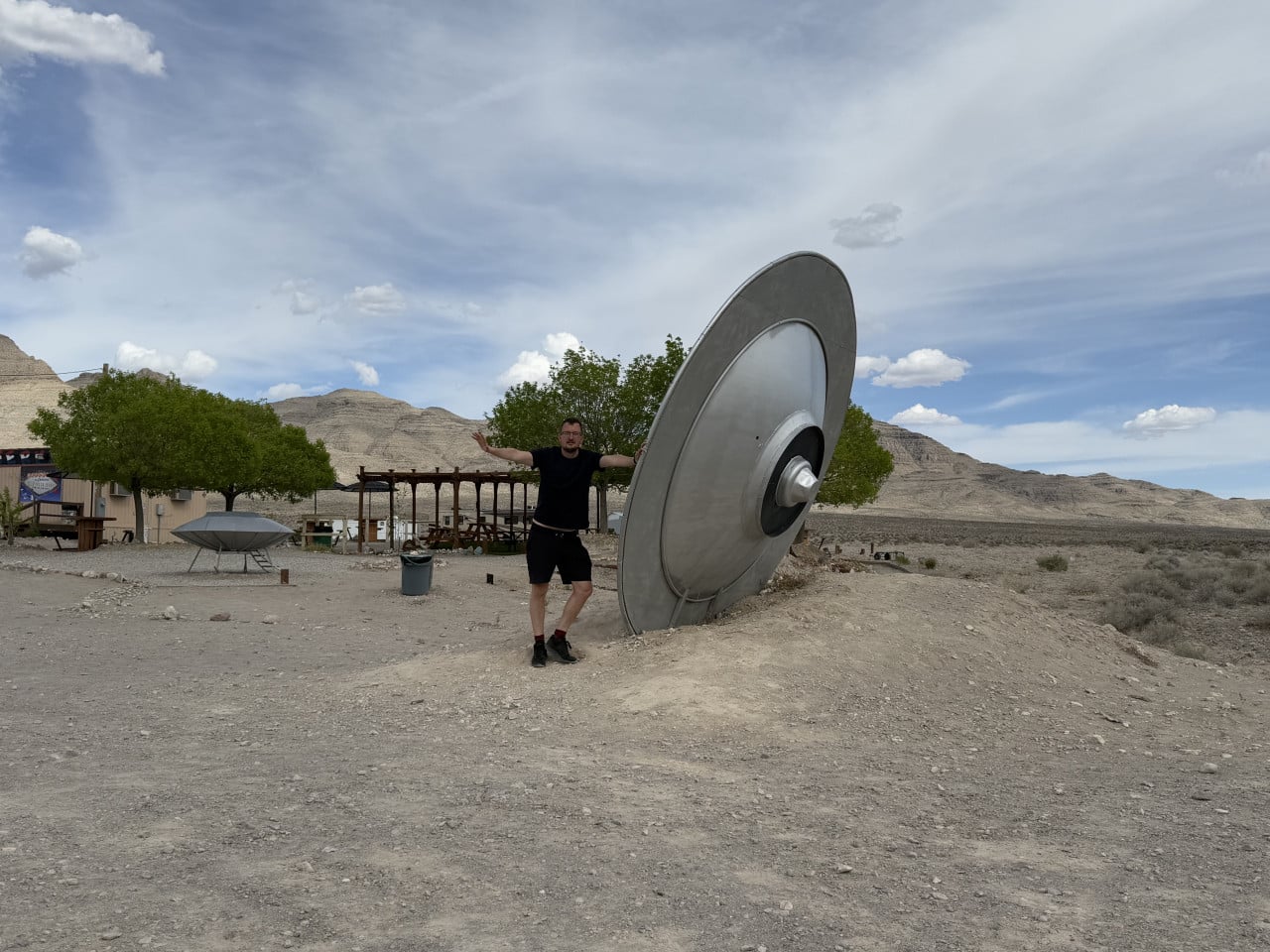 Muž stojí u obřího modelu UFO v pouštní krajině Nevady.