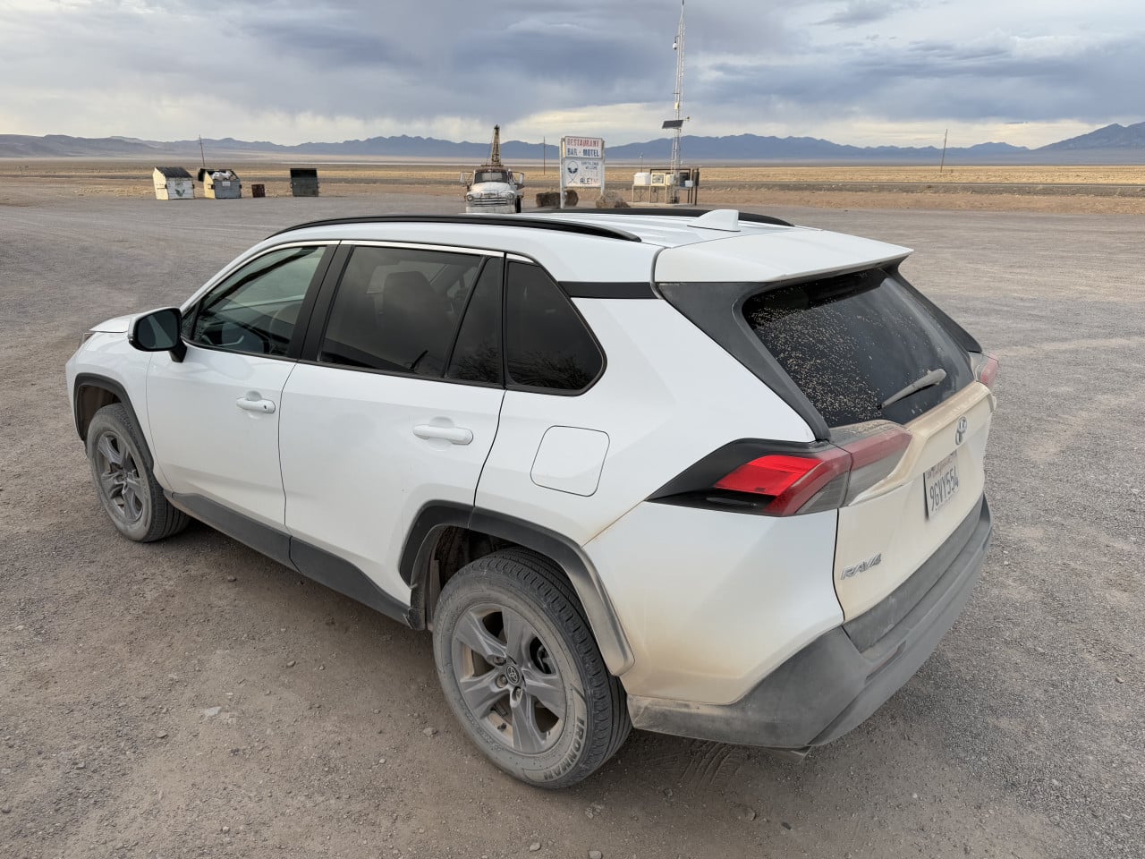 Bílé SUV na prašné planině u silnice, v pozadí cedule a horská krajina Nevadské pouště