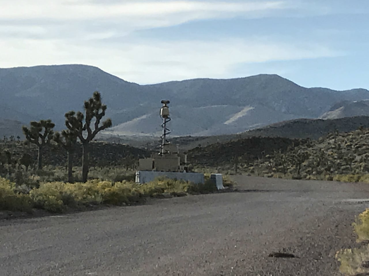 Pouštní cesta k bráně Area 51 s kamerovým stožárem a horami v pozadí