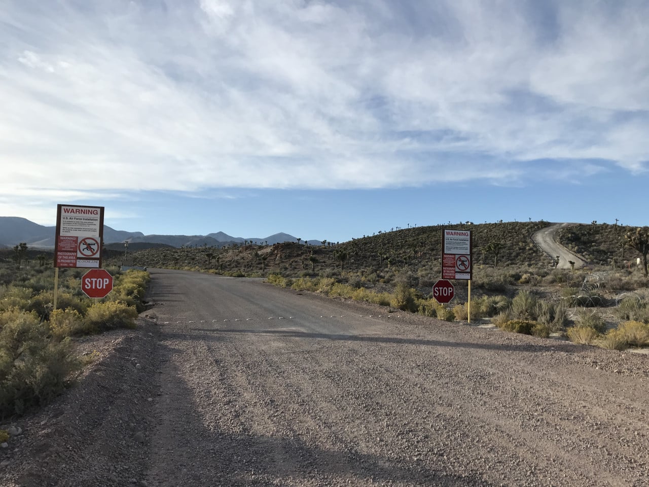 Prašná silnice k bráně Area 51 s výstražnými cedulemi a stop značkami v poušti.