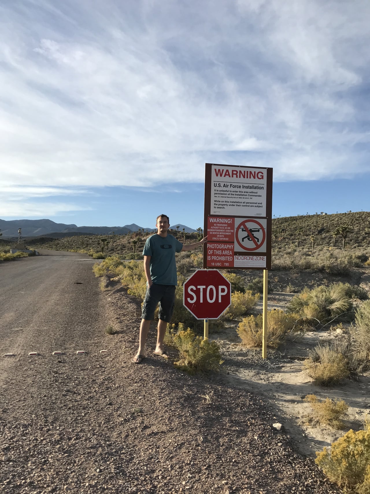 Muž stojí u brány Area 51 vedle varovných značek a stop značky.