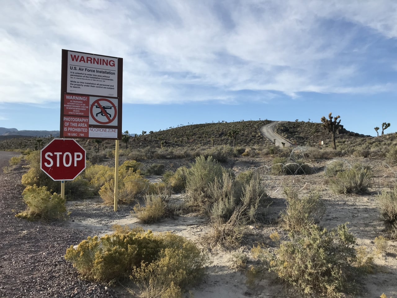 Výstražná cedule u Area 51, stopka a pouštní cesta v Nevadě