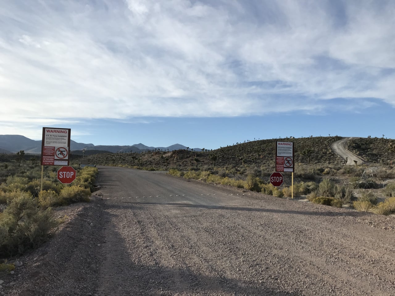 Prašná cesta k bráně Area 51 se zákazovými cedulemi a stop značkami