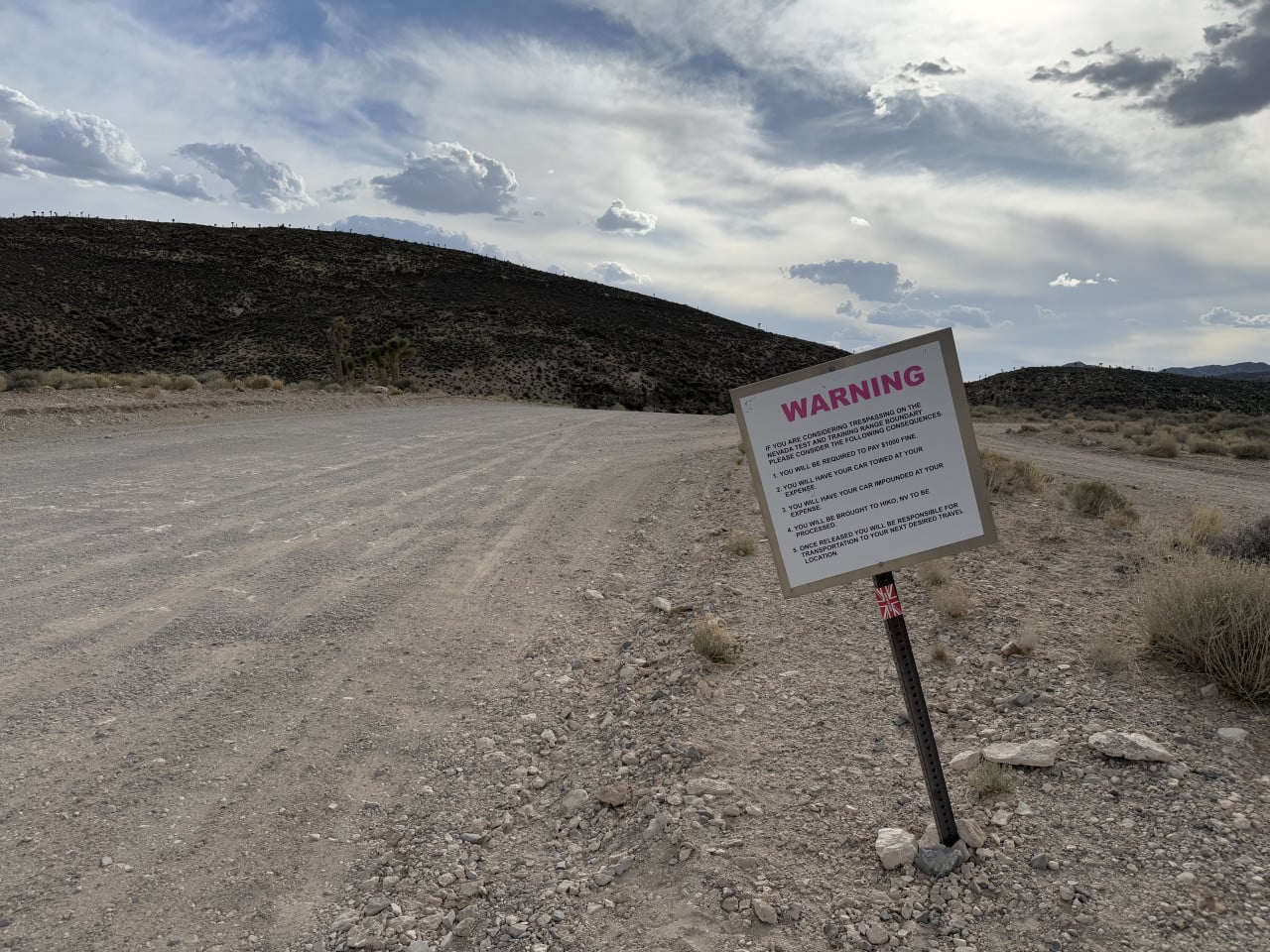 Pouštní cesta u Area 51 s výstražnou cedulí WARNING a kopci v pozadí