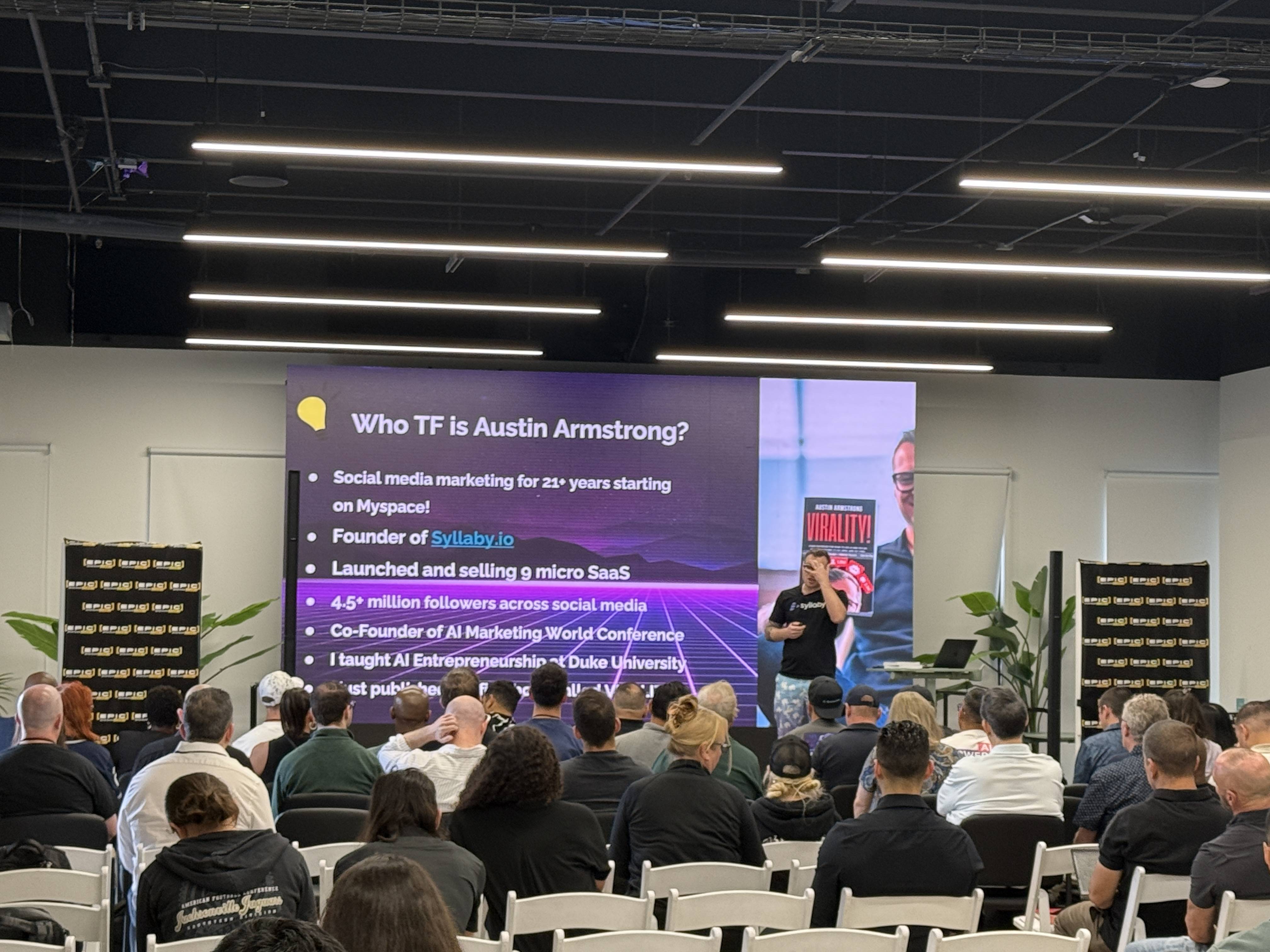 Přednášející na pódiu, publikum, slide Who TF is Austin Armstrong? a Syllaby.io.