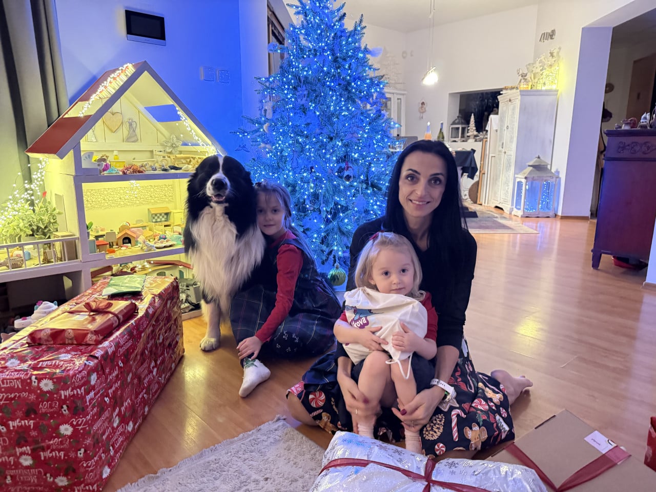 Žena se dvěma dětmi a australským ovčákem u modře svítícího vánočního stromku.