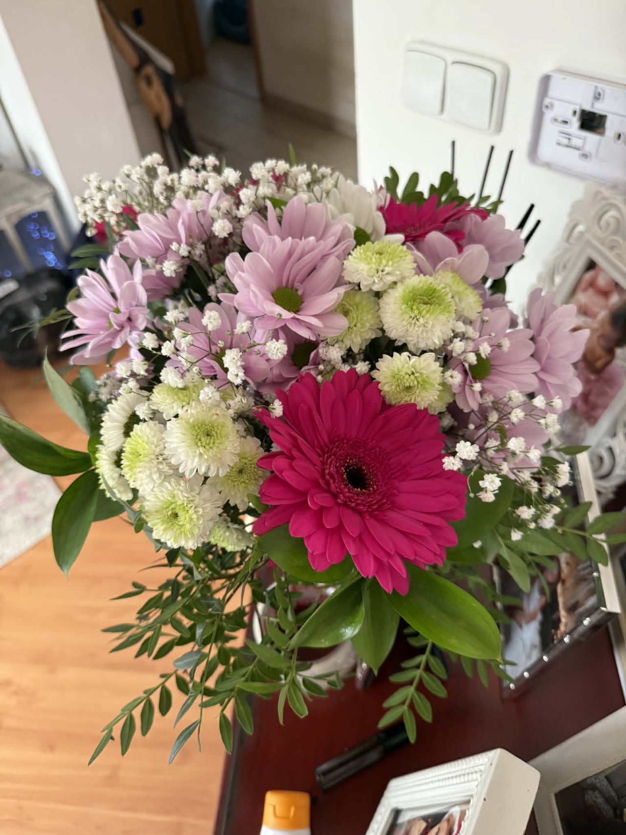 Barevná kytice růžových a bílých chryzantém s fuchsiovou gerberou v interiéru.