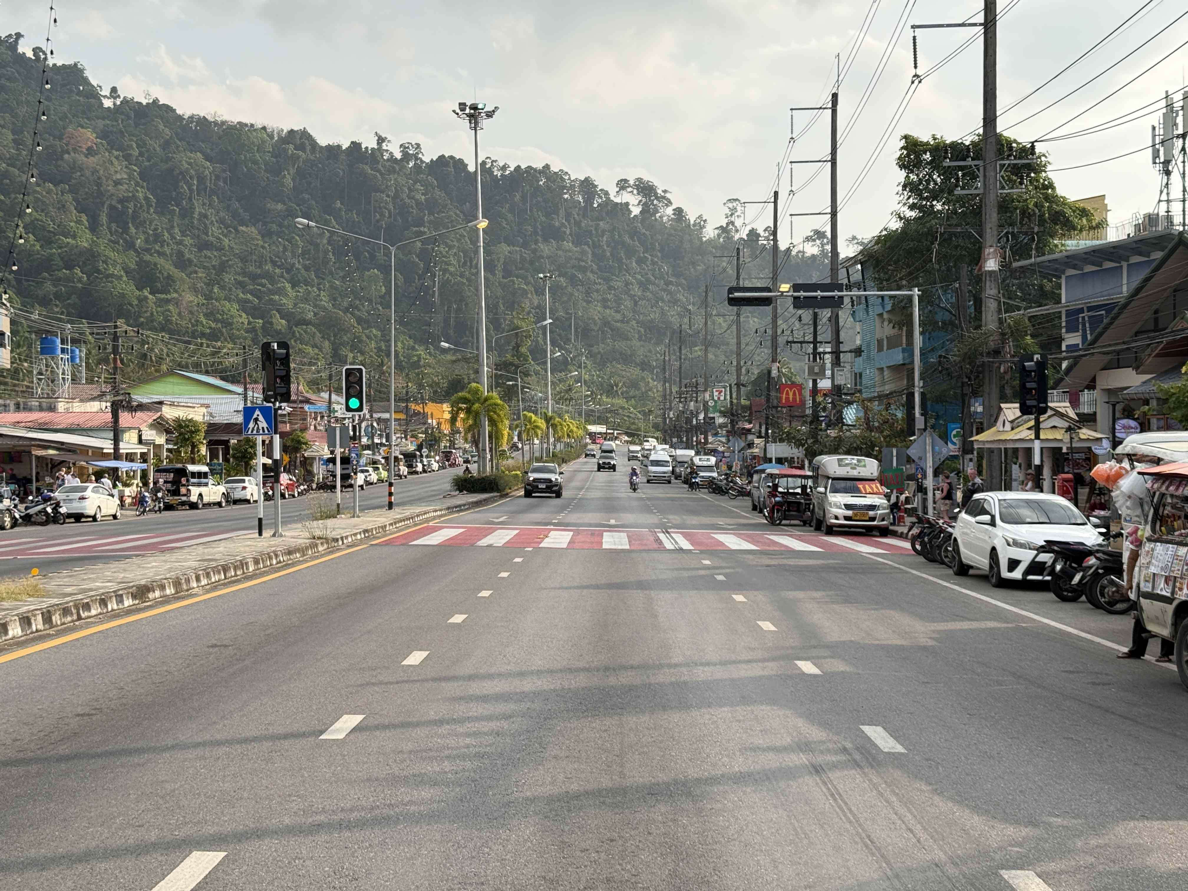 Hlavní silnice v Khao Laku, auta a motorky, v pozadí hory, cedule 7 a McDonald's