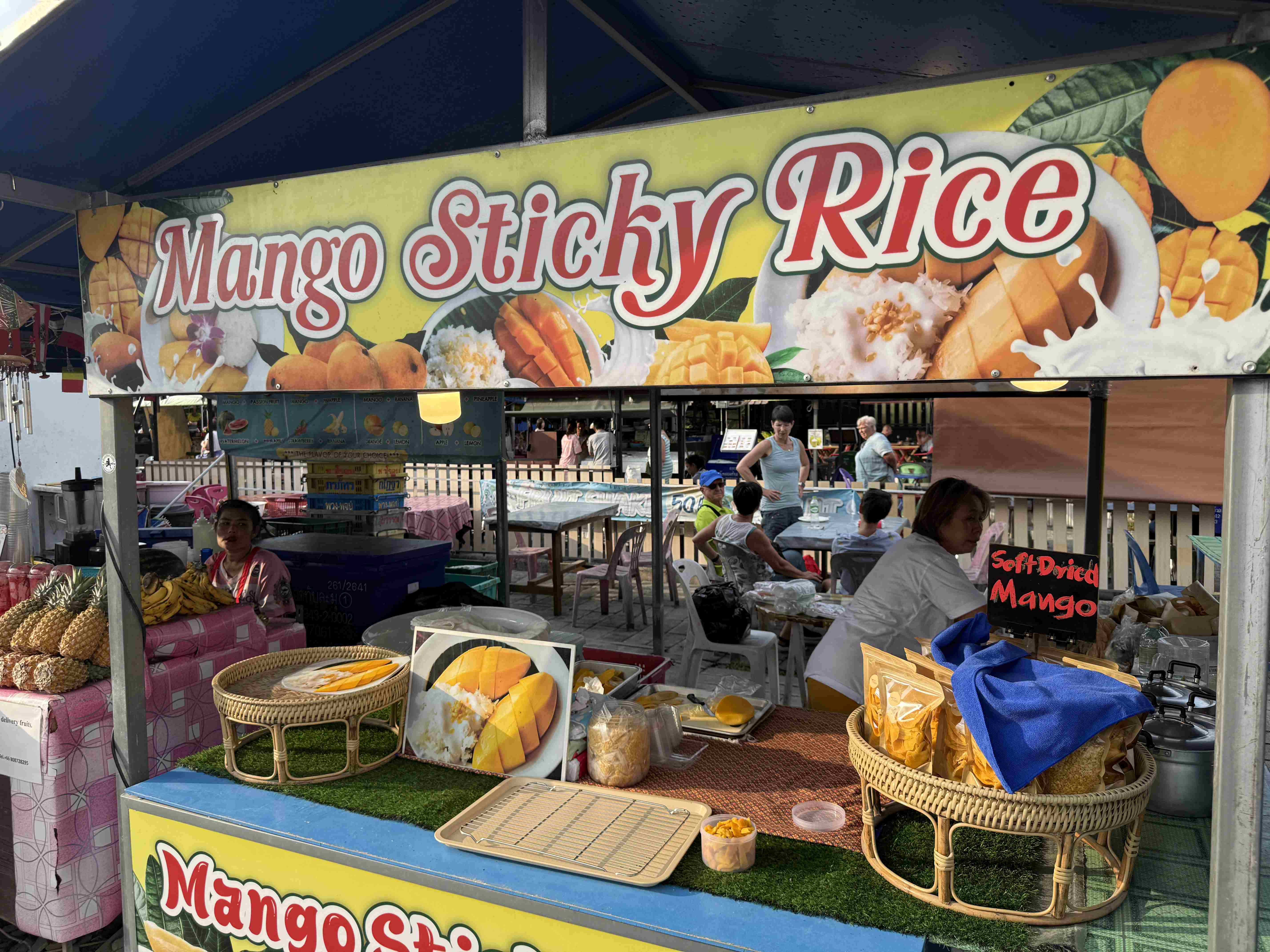 Stánek s nápisem Mango Sticky Rice, ovoce a cedule Soft Dried Mango.