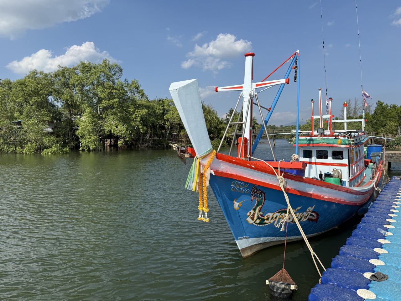 Modro-červená loď s thajským nápisem a čísly 6754 0930 kotví u mola.