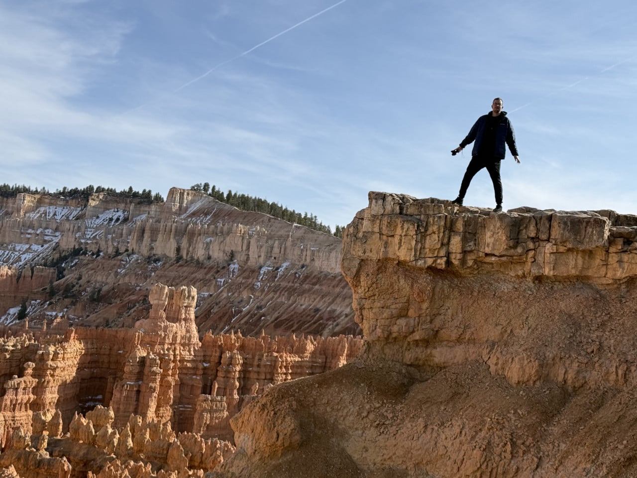 Muž stojí na skalním převisu nad oranžovými hoodoos v Bryce Canyonu