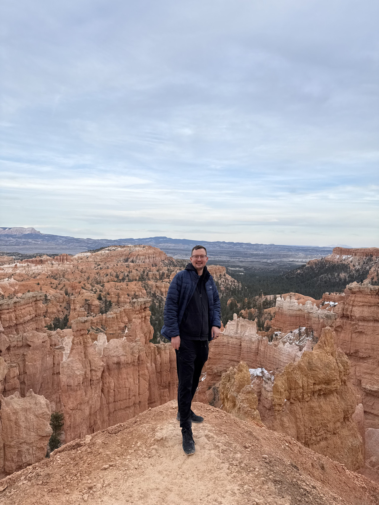 Muž v bundě stojí na vyhlídce nad oranžovými skalními věžemi Bryce Canyonu.