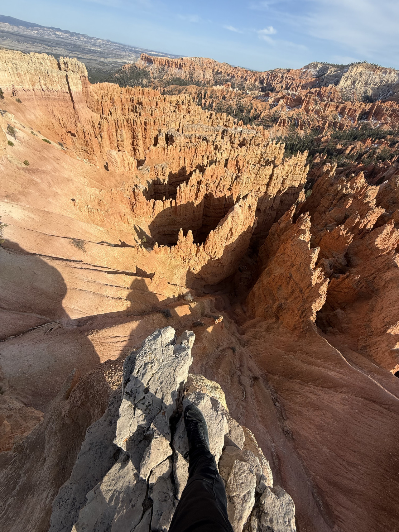 Pohled z okraje Bryce Canyonu na oranžové skalní věže, noha na skále