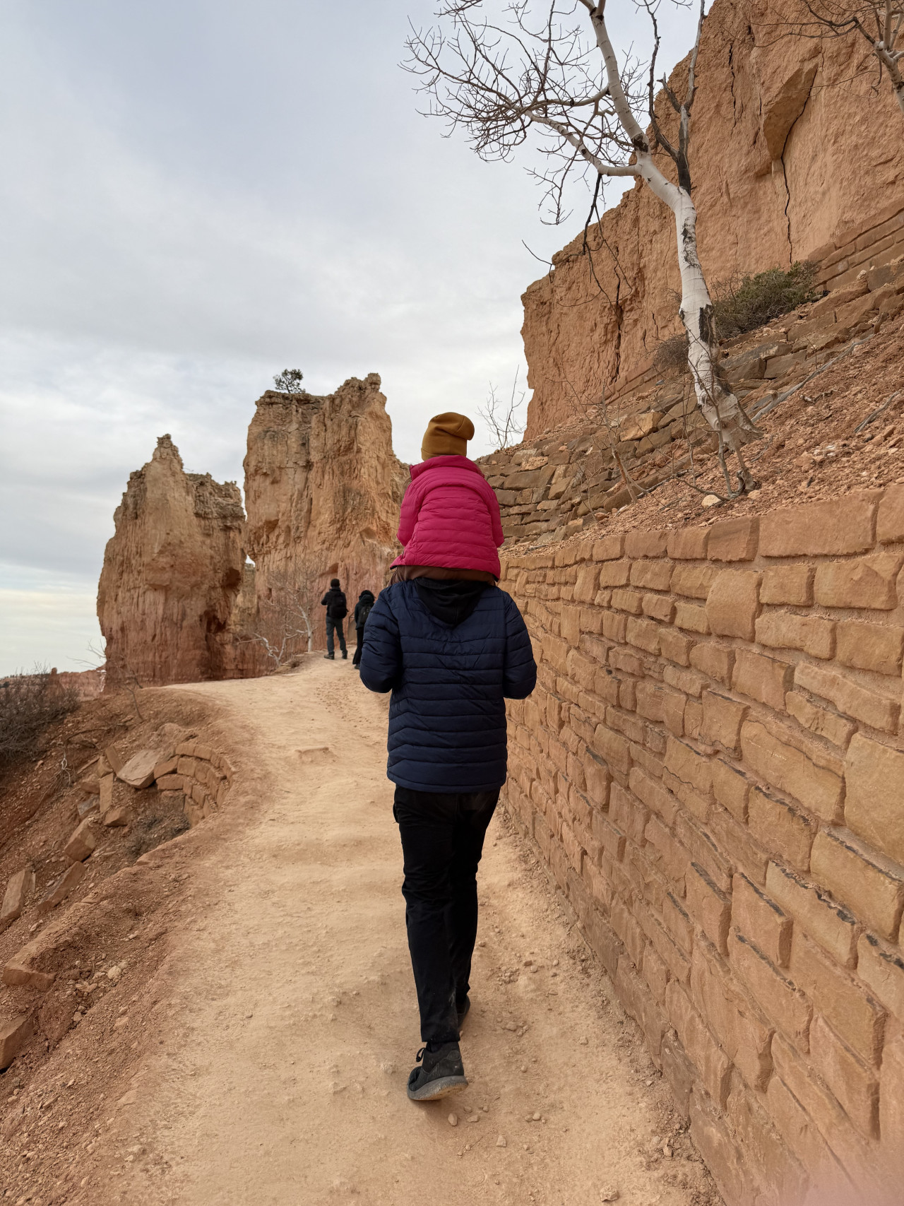 Turista nese dítě na ramenou po stezce mezi skalními věžemi Bryce Canyonu