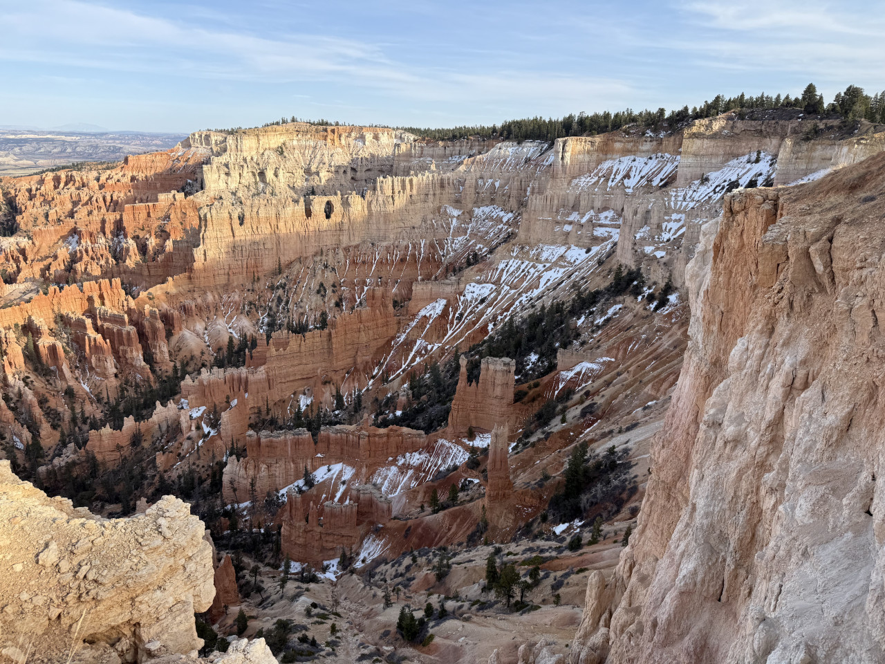 Panorama Bryce Canyonu s pískovcovými věžemi, útesy, sněhovými pásy a borovicemi.