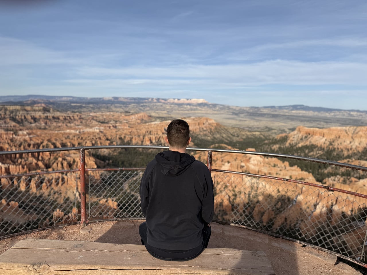Muž sedící na vyhlídce, zády k fotoaparátu, s výhledem na Bryce Canyon
