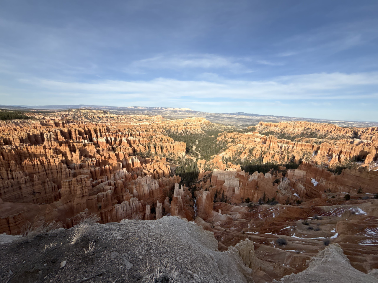 Panoramatický výhled na oranžové skalní věže Bryce Canyonu pod modrou oblohou.