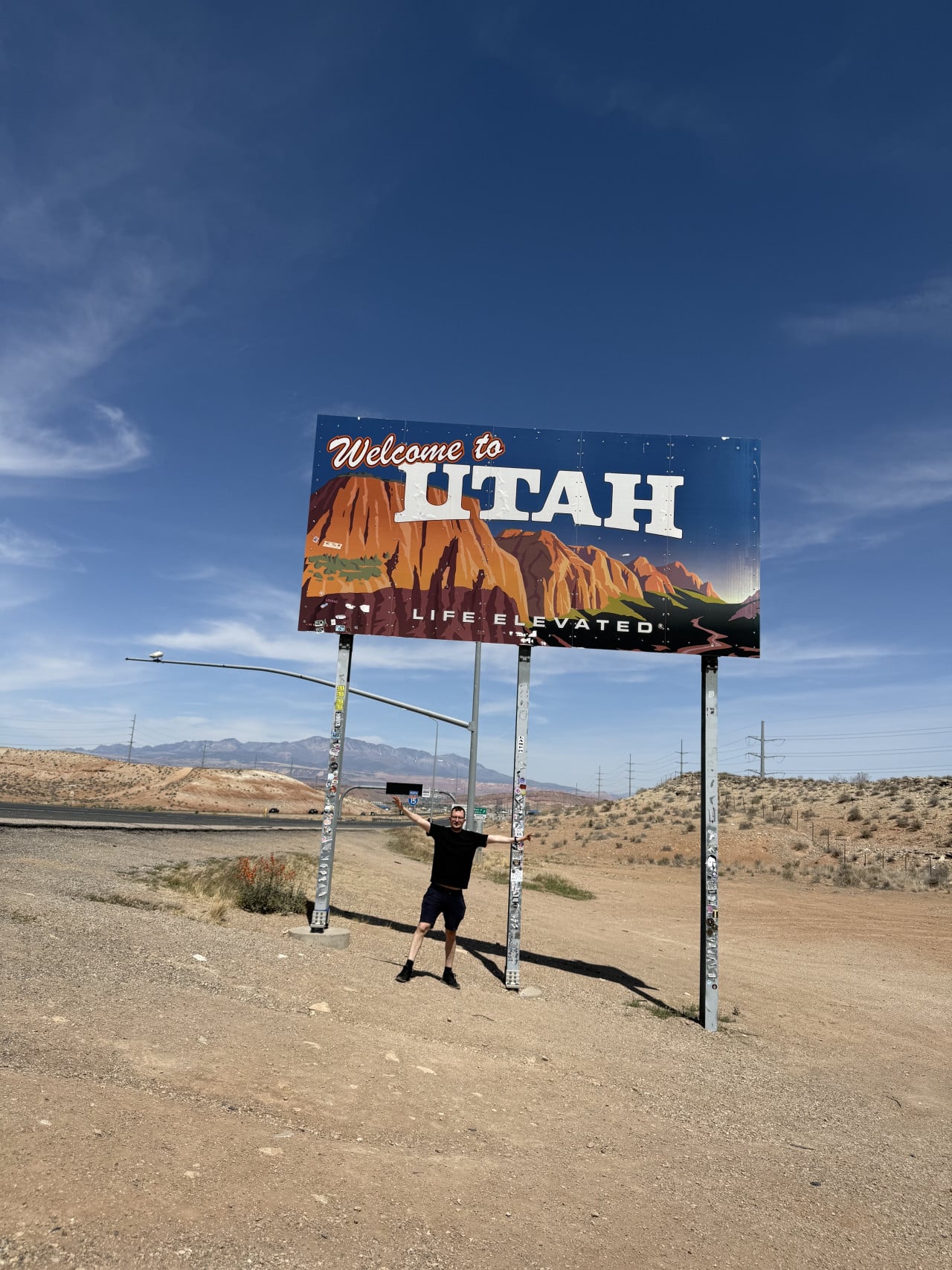 Muž pod billboardem Welcome to UTAH, LIFE ELEVATED u silnice v poušti.