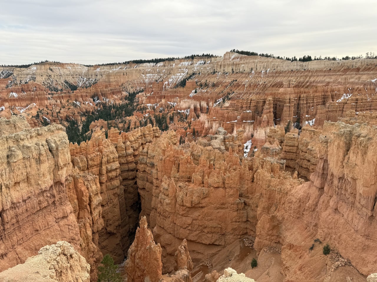 Skalní věže hoodoo v Bryce Canyonu, zasněžené svahy a zatažená obloha