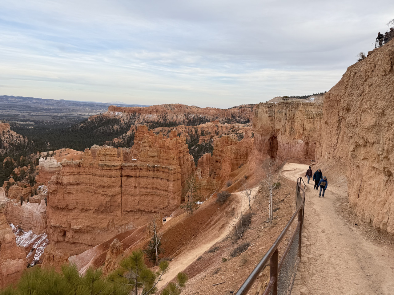 Stezka s turisty u skalní stěny, výhled na červené hoodoos Bryce Canyonu.