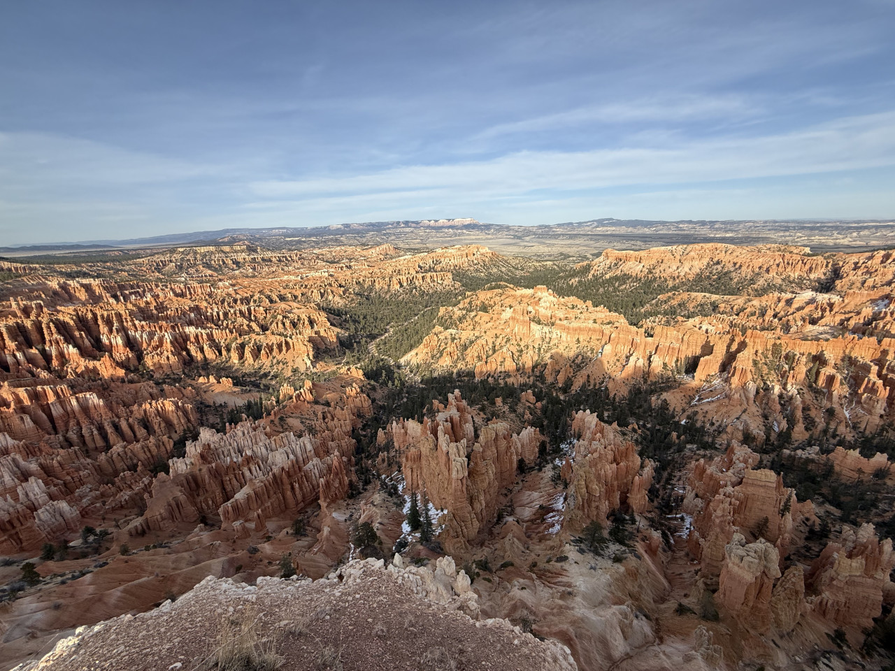 Panoramatický výhled na oranžové hoodoos Bryce Canyonu, borovice a zbytky sněhu.